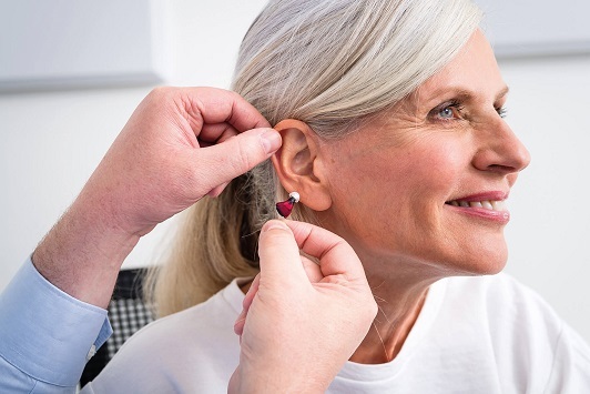 Seniorin bekommt ein modernes Hörgerät ins Ohr eingesetzt, Hörgeräte Anpassung.